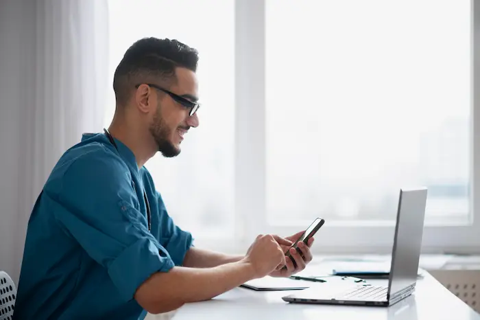 Ejecutivo trabajando en networking digital desde una oficina, usando celular y laptop para conectar y construir relaciones profesionales.