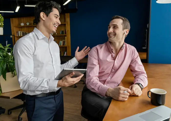 Dos ejecutivos en una reunión de networking, conversando y compartiendo ideas con tablet en una oficina moderna, perfectos para consejos de networking