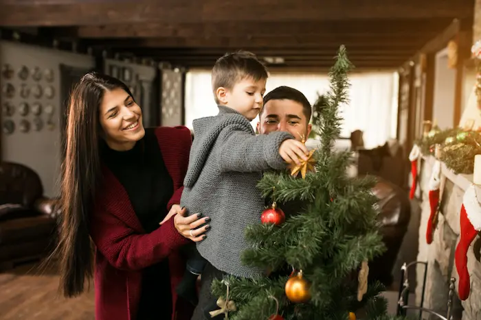 niño decorando el arbol de navidad junto a sus padres